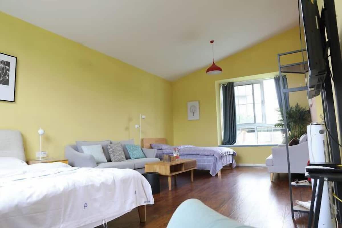 A room with two beds, a sofa, a small table, a TV, and a window.