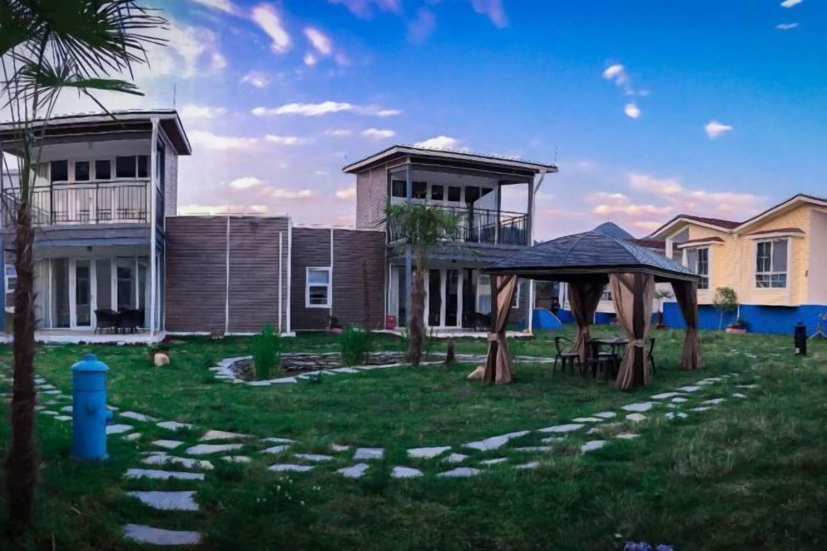 A residential area with a gazebo, a covered outdoor seating area, and a pathway leading to a building with a balcony.