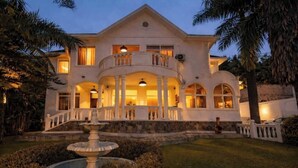 A large, two-story building with a central balcony, a fountain in the foreground, and a well-maintained garden. - Amata n’Ubuki : Single – IGAJU (Kigali)