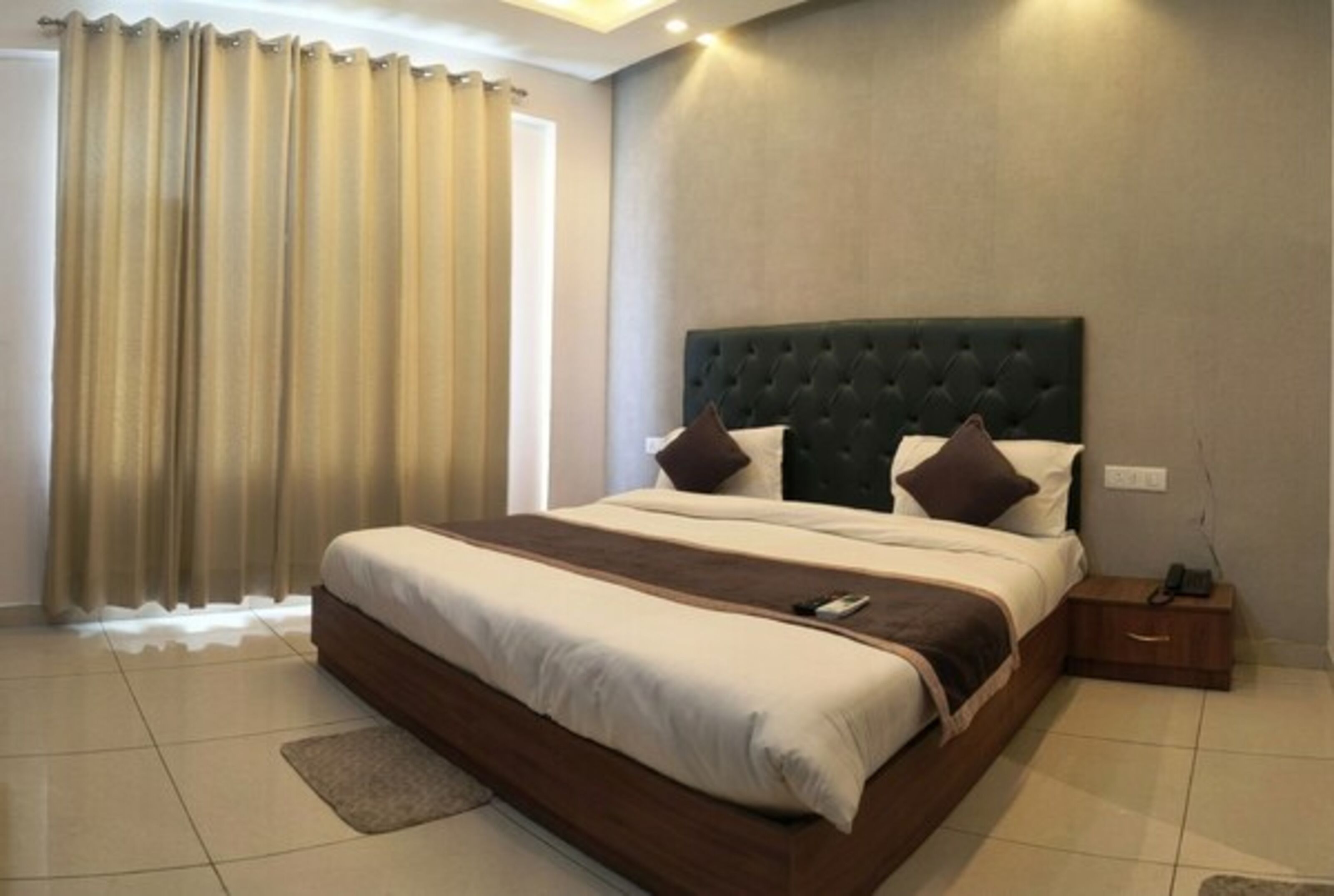 A hotel room with a large bed, a bedside table, a nightstand, and a window with curtains.