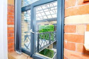 Ein Fenster mit Metallrahmen, eine Ziegelwand und Blick auf einen grünen Heckenstreifen.