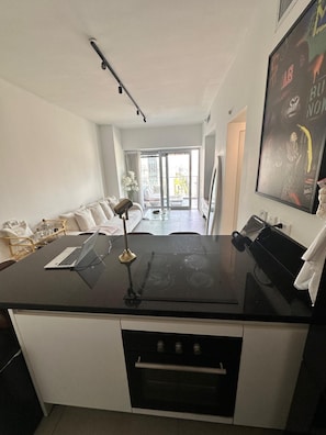 Ett modernt kök med en svart bänkskiva, vita skåp, en inbyggd ugn och en matplats med en vit soffa och ett glasbord.