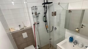 Ett modernt badrum med en dusch som är avskärmad med glasväggar, ett vitt handfat och en toalett.
