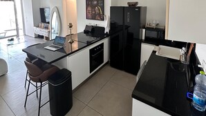 Ett modernt kök med ett svart kylskåp, en mikrovågsugn och en matplats med ett bord och stolar i glas.