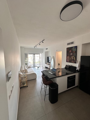 Een moderne keuken met een centraal eiland, een zithoek met een bank en een groot raam dat voor natuurlijk licht zorgt.