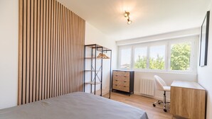 A bedroom with a bed, a desk, a chair, a radiator, and a window with a view of trees.
