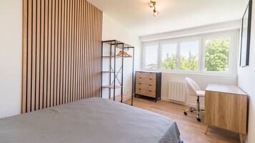 Une chambre à coucher comprenant un lit, un bureau, une chaise, un radiateur et une fenêtre donnant sur des arbres.