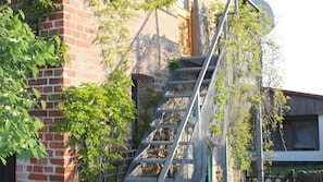 Ein Backsteinhaus mit Metalltreppe und Kletterpflanzen.