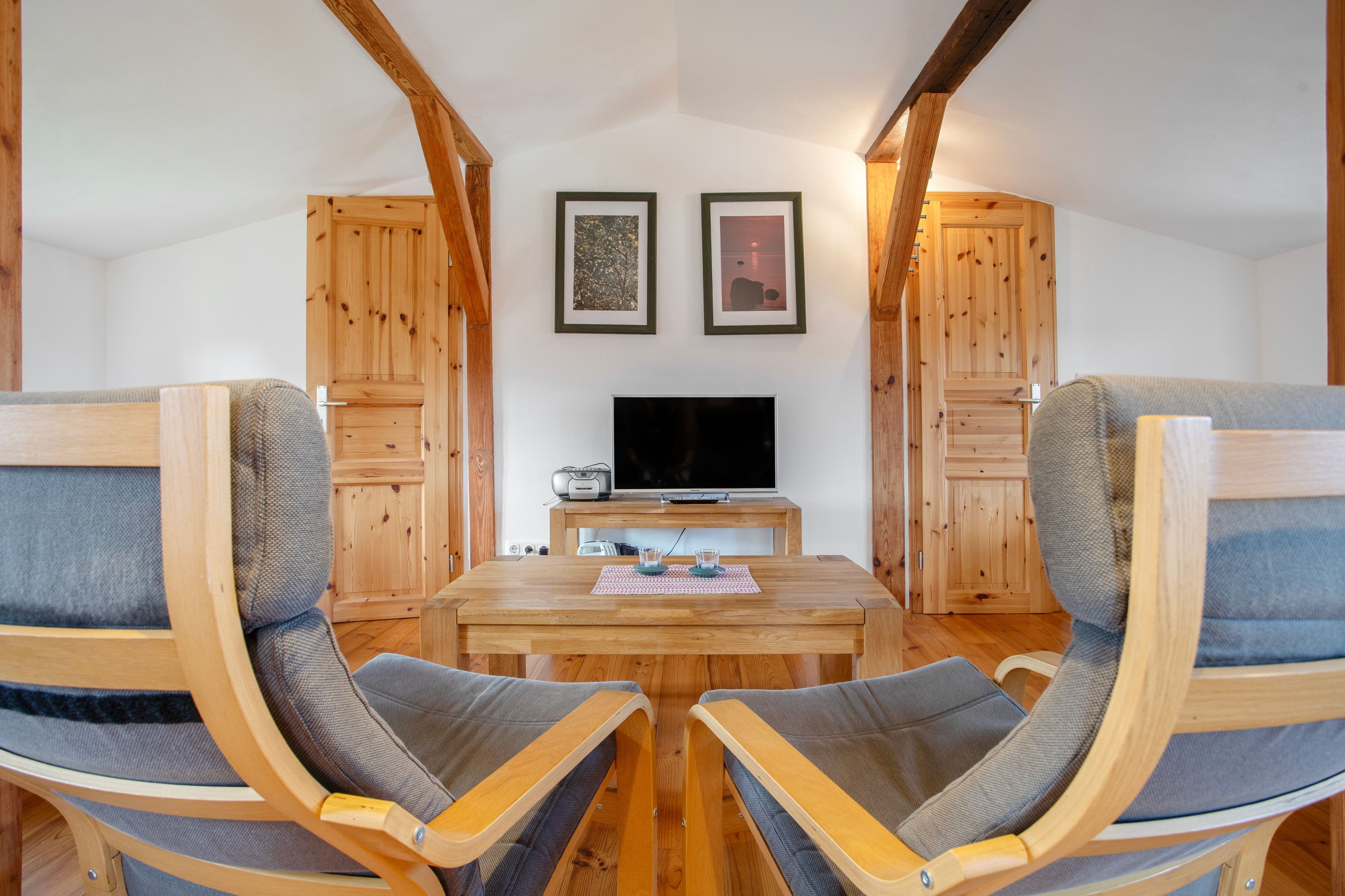 Ein gemütliches Zimmer mit Holzmöbeln, einem Fernseher und zwei gerahmten Bildern an der Wand.