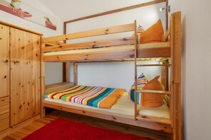 Ein Etagenbett mit Holzrahmen, ein roter Teppich und ein kleiner Schrank.