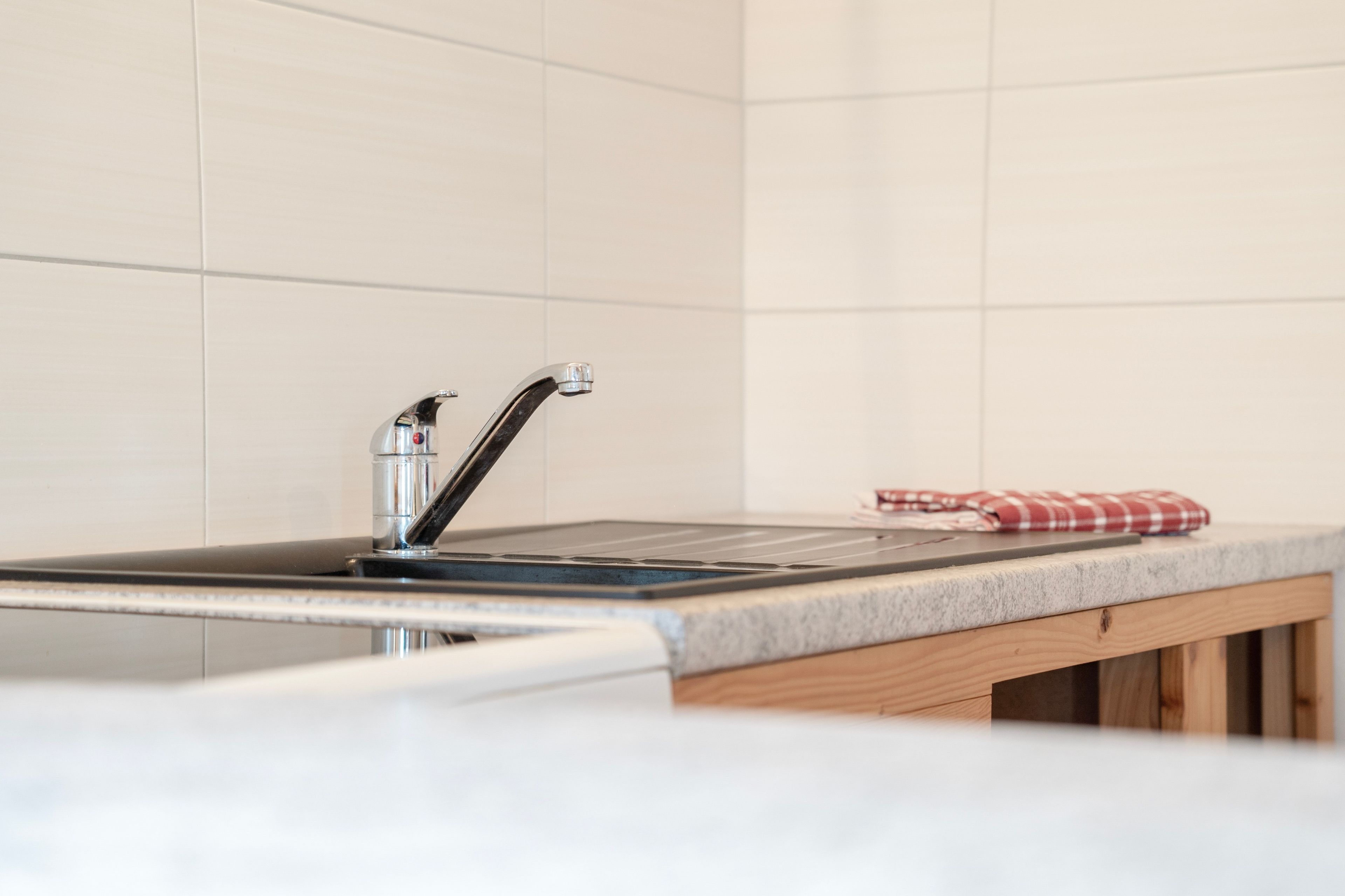Una cocina con un lavamanos de acero inoxidable, una encimera de madera y un mantel a cuadros rojo y blanco.
