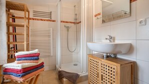 A bathroom with a shower, a sink, a wooden cabinet, and a towel rack with towels. - Apartment "Galerie" – Cozy Retreat Near Water and Forest (Kröslin)