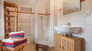 Ein Badezimmer mit Dusche, Waschbecken, einem Holzkabinent und einem Handtuchhalter mit Handtüchern.