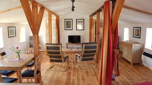 Ein Zimmer mit Esstisch aus Holz, zwei Stühlen, einem Fernseher und einer Küchenzeile.