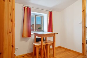 Ein kleiner Raum mit einem Holztisch und zwei Stühlen, ein Fenster mit Blick auf Gebäude und einem Vorhang.