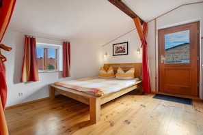 Un dormitorio con cama de madera, ventana con cortinas, una puerta y una lámpara fijada a la pared.