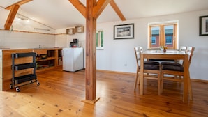A spacious kitchen with wooden beams, a dining area with a table and chairs, and a refrigerator. - Apartment "Galerie" – Cozy Retreat Near Water and Forest (Kröslin)