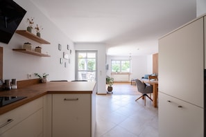 Una cocina moderna con estantes de madera, un comedor con mesa y sillas, y vista al exterior.