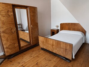 Ein Schlafzimmer mit einem hölzernen Bett, einem Holzschrank mit Spiegel, einem Nachttisch und einem Beistelltisch.