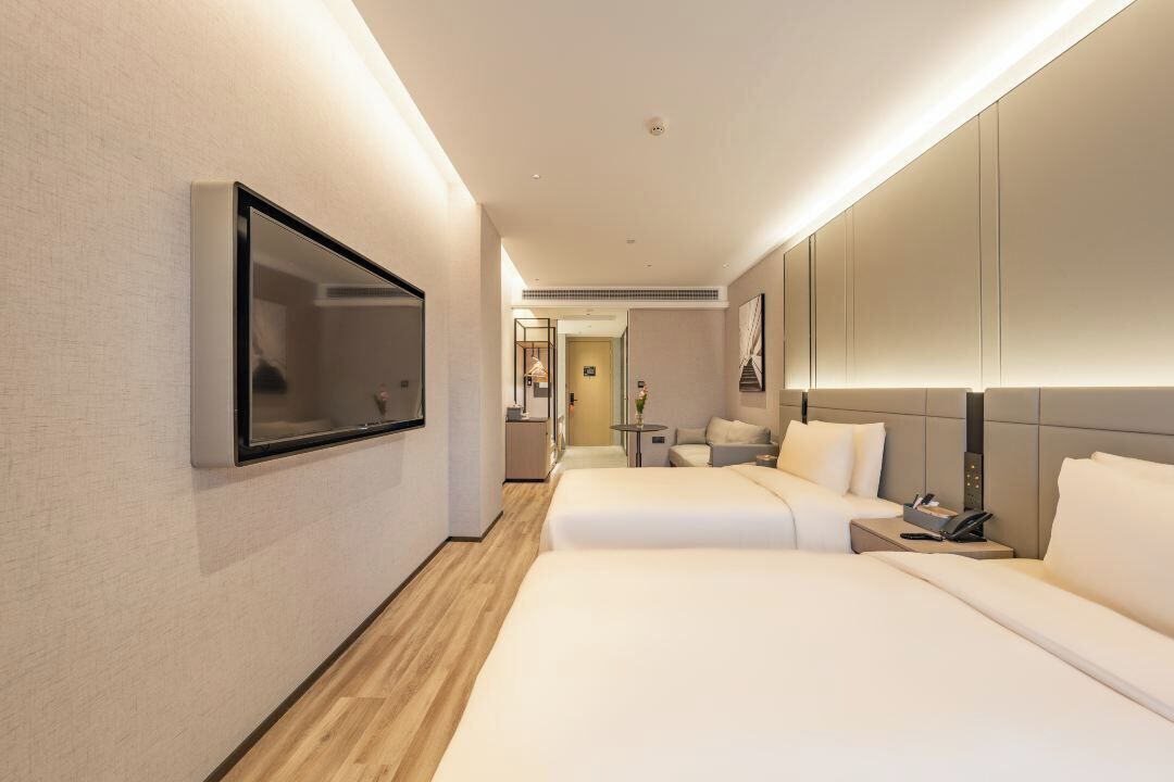 Et moderne hotelværelse med to senge, et fladskærms-tv, et natbord med telefon og et lille bord med lampe.