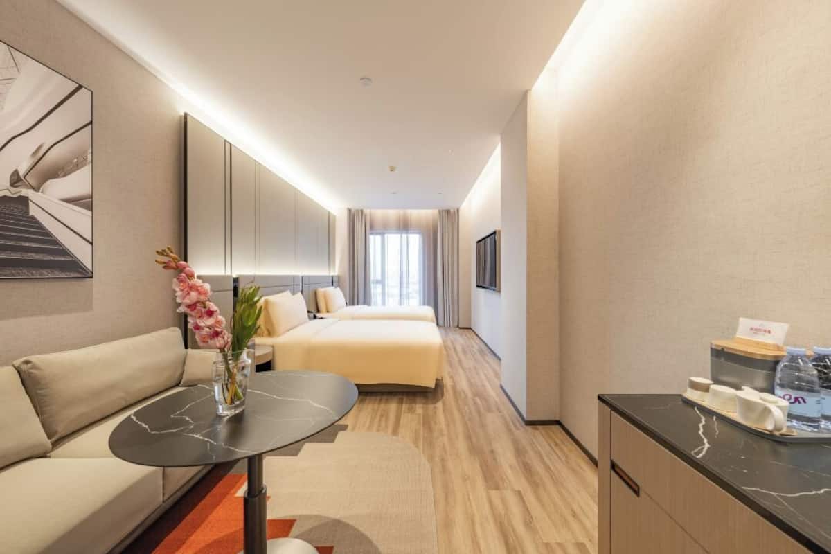 Habitación de hotel con cama, sofá, una mesita, espejo, televisor y un mueble de baño con artículos de aseo.