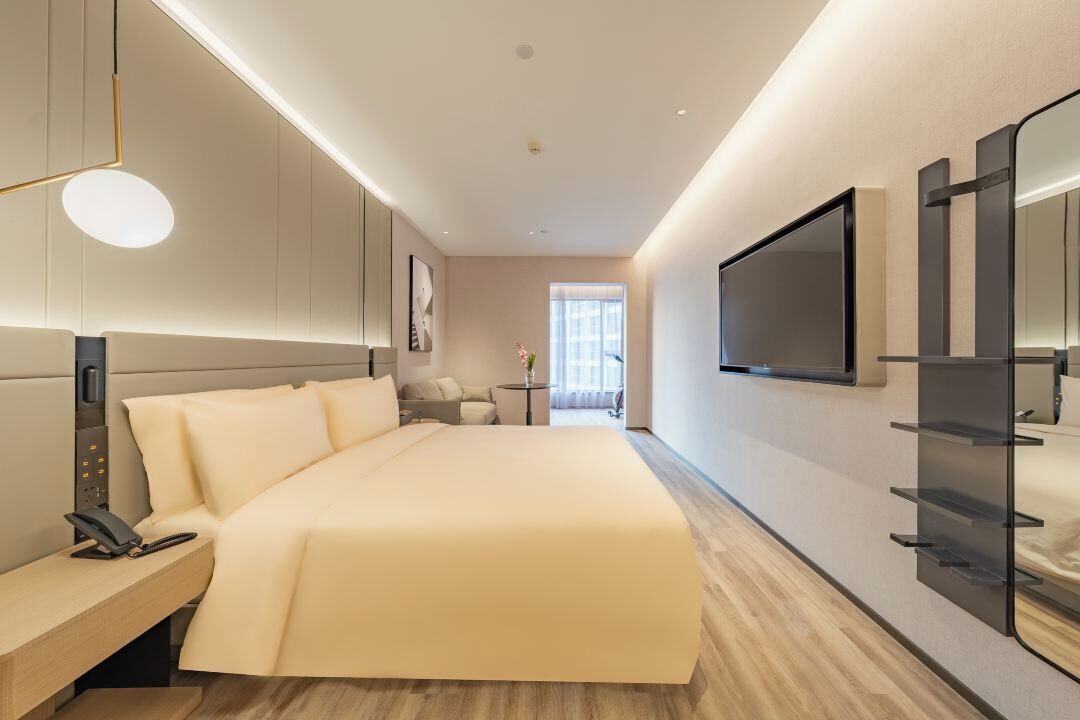 Una habitación de hotel moderna con una cama grande, mesita de noche y un televisor montado en la pared.