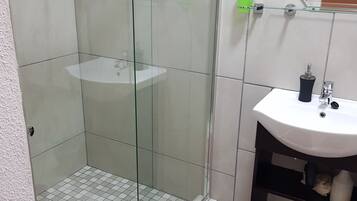 A bathroom with a glass shower enclosure, a white sink, and a red bath mat.