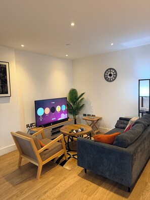 Ein modernes Wohnzimmer mit Flachbildfernseher, Spielkonsole, Sofa, Couchtisch und einer Pflanze.