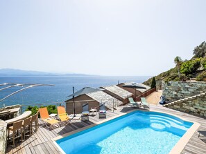 A swimming pool with lounge chairs and a view of the sea.