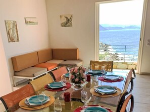 A dining area with a table set for four, a sofa, and a view of the sea.