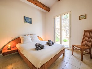 A bedroom with a bed, a chair, a nightstand, a painting, and a window. - Kanelata by Interhome (Canari)