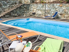 A swimming pool with stone steps, lounge chairs, and a table with a drink and a cake. - Kanelata by Interhome (Canari)