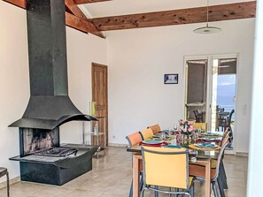 A dining area with a large black stove, wooden beams, a door leading outside, and a table set for dining.
