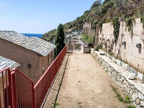 A narrow pathway leading to a building with a tiled roof and a stone wall with vegetation. - Kanelata by Interhome (Canari)