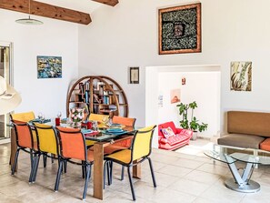 A dining area with a round table, colorful chairs, a bookshelf, and a red chair with a bag. - Kanelata by Interhome (Canari)