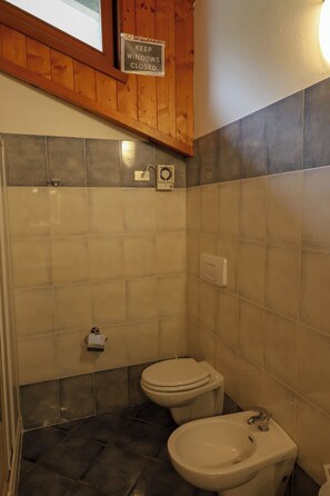 Un baño con inodoro, bidé y un cartel que indica mantener las ventanas cerradas.