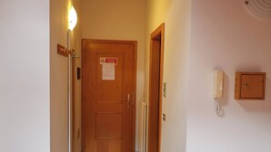 A hallway with a wooden door at the end, a light switch, and a wall-mounted telephone. - Apartment 12 Maso Anna (Mastellina)