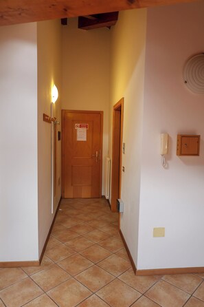 Un pasillo con una puerta de madera al final, un interruptor de luz y un teléfono instalado en la pared.