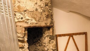 A stone wall with a fireplace, a metal door, and a wooden frame leaning against the wall. - Apartment 12 Maso Anna (Mastellina)