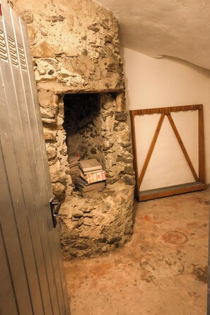 Un muro de piedra con una chimenea, una puerta metálica y un marco de madera apoyado contra la pared.