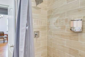 Ein Badezimmer mit beigen Fliesen, einer Duschvorhang und einem wandmontierten Seifenspender.