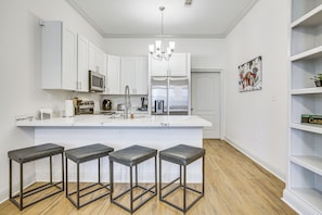 Eine moderne Küche mit weißen Schränken, einem Edelstahl-Kühlschrank, einer Mikrowelle und einer Bar mit Sitzgelegenheit.