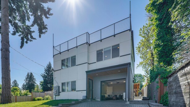 A modern two-story building with a flat roof, a balcony on the upper floor, and a driveway leading to the entrance. - Rooftop Deck + Private Patio! West Seattle Home (Seattle)