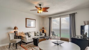 Een moderne woonkamer met een ronde eettafel, een bank, een plafondventilator en een balkon met uitzicht.