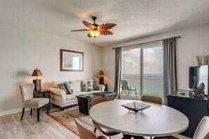 Een moderne woonkamer met een ronde eettafel, een bank, een plafondventilator en een balkon met uitzicht.
