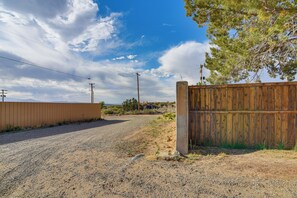 A gravel road leading to a wooden fence with a metal gate, surrounded by sparse vegetation and utility poles.