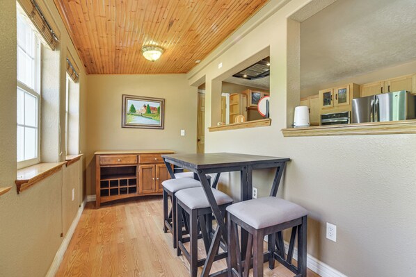 A kitchen with wooden cabinets, a refrigerator, and a dining area with a table and stools.