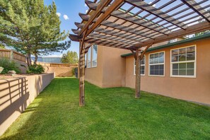 A covered patio area with a pergola, a well-maintained lawn, and a building with windows.