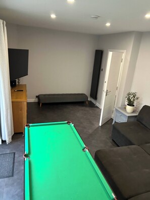 A pool table, a sofa, a television, and a door leading to another room.