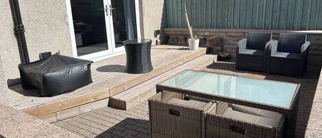 An outdoor patio with wicker furniture, a glass-top table, and a covered seating area.